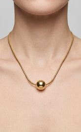 Gold necklace with a round pendant on a neutral background