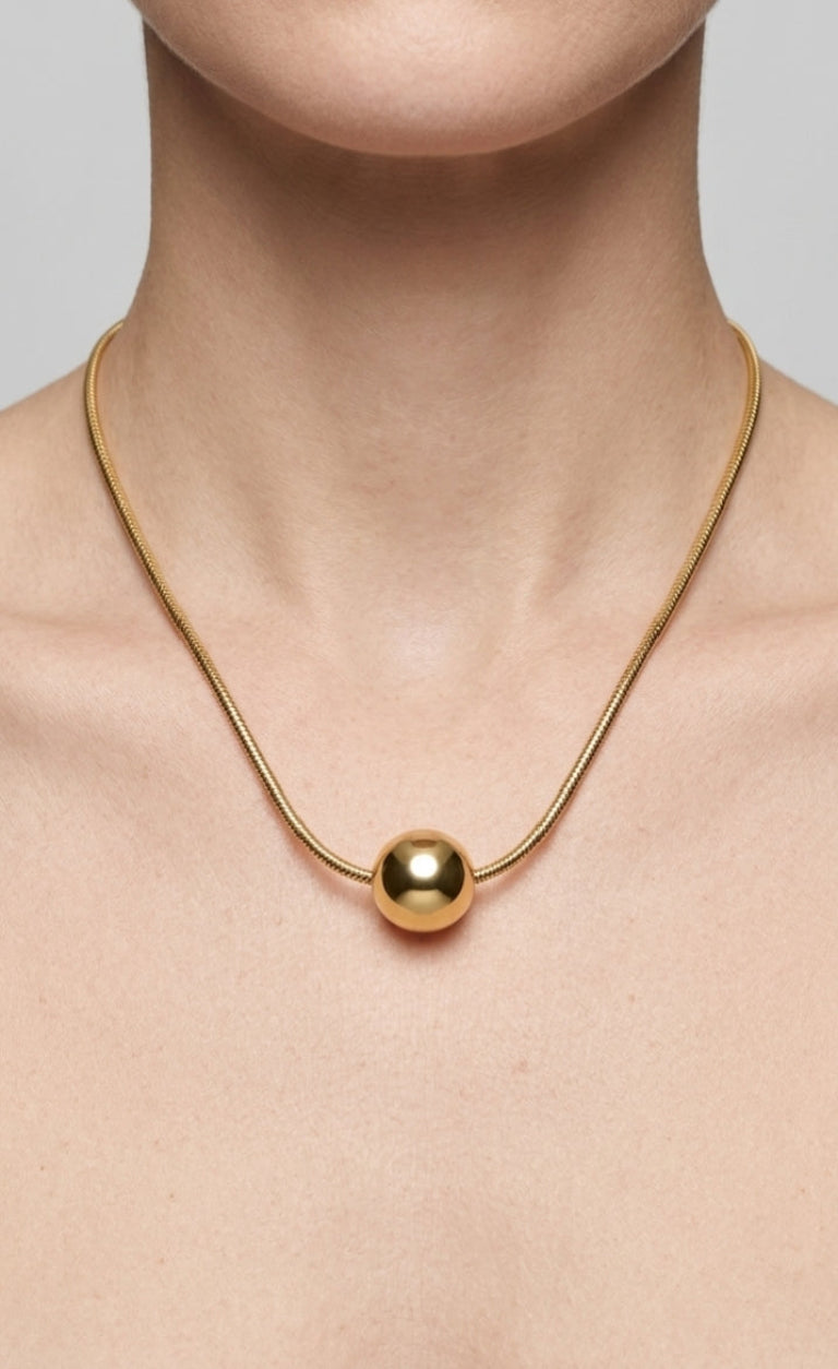 Gold necklace with a round pendant on a neutral background