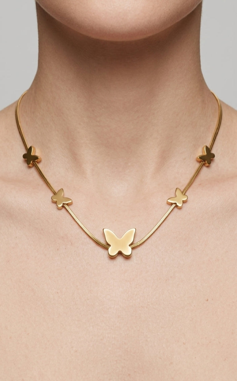 Gold butterfly necklace on a person's neck against a neutral background