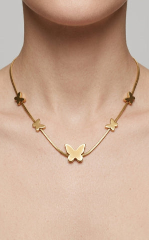 Gold butterfly necklace on a person's neck against a neutral background