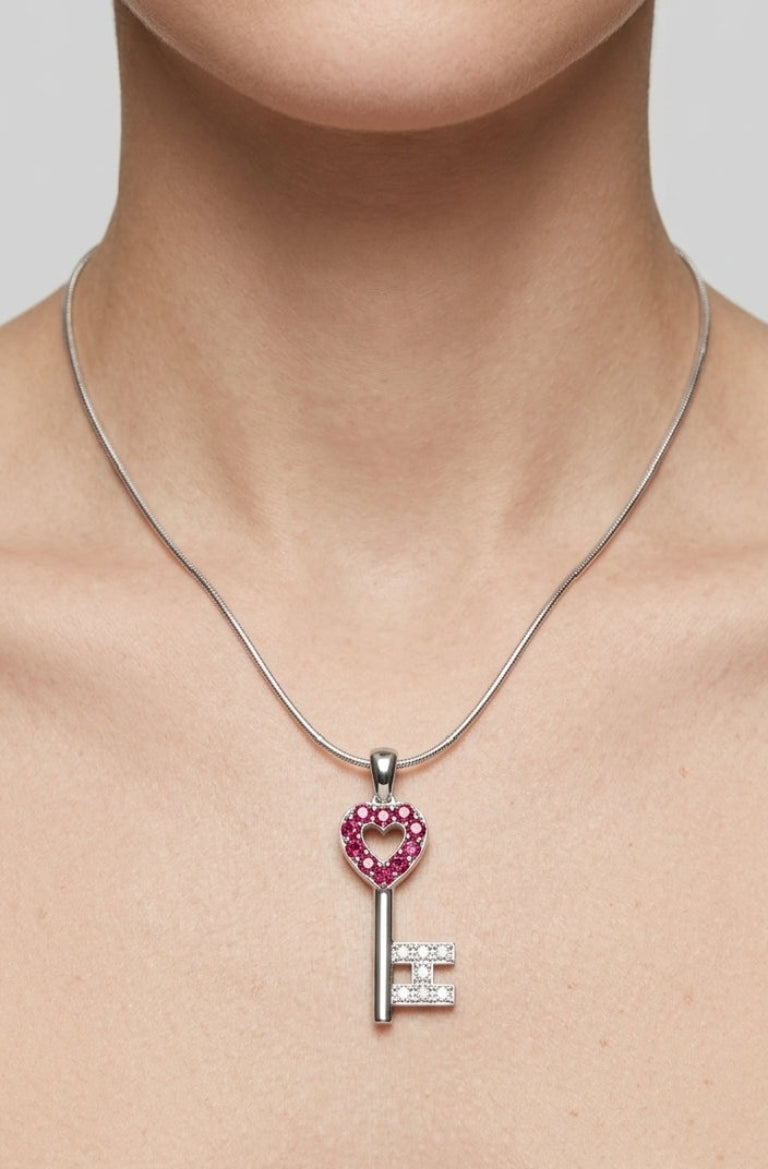 Silver key-shaped pendant with heart design and gemstones on a necklace against a neutral background
