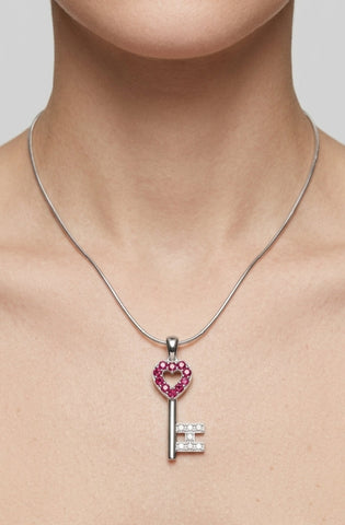 Silver key-shaped pendant with heart design and gemstones on a necklace against a neutral background
