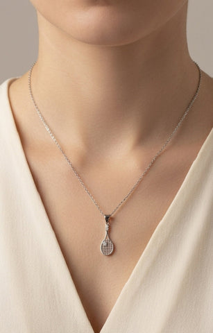 Necklace with a tennis racket pendant worn by a person in a beige top.