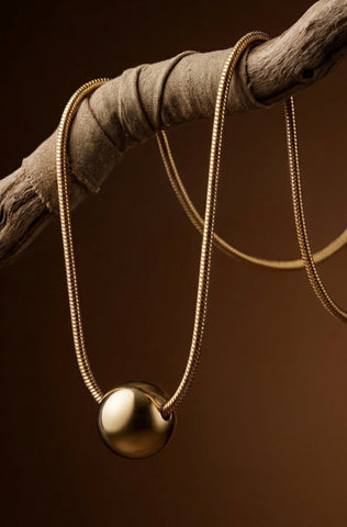 Gold necklace with a spherical pendant on a wooden branch against a brown background