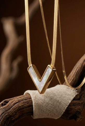 Gold necklace with a V-shaped pendant on a wooden branch