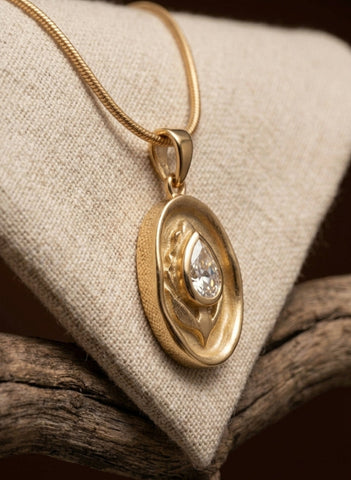 Gold pendant with a diamond on a beige fabric background